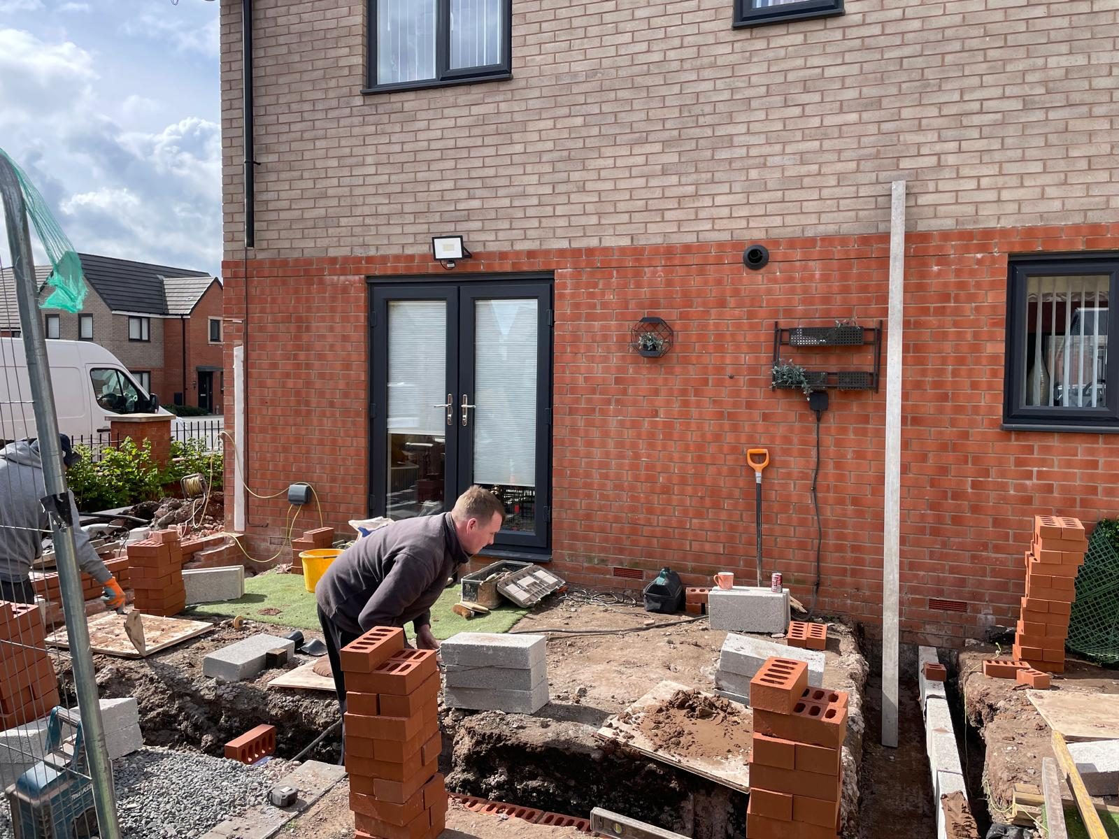 Foundations being dug and bricks laid for a rear patio at the back of a brick built home