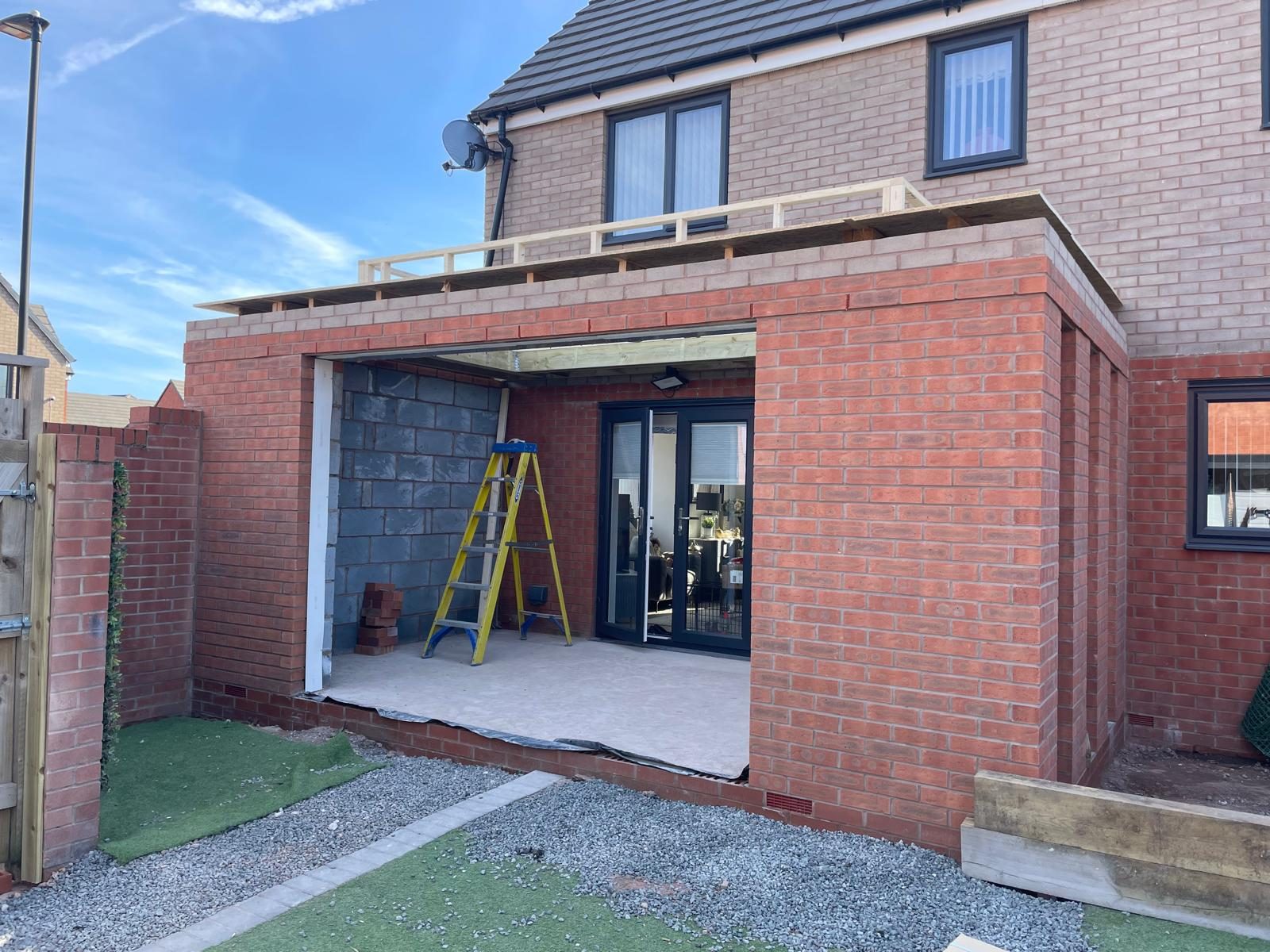 Single storey rear extension part built in red brick with the roof timbers exposed and an open doorway