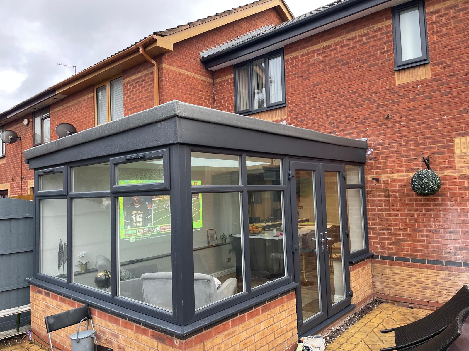 Rebuilt garden room with anthracite grey frames, French doors and a flat solid roof on a red brick house