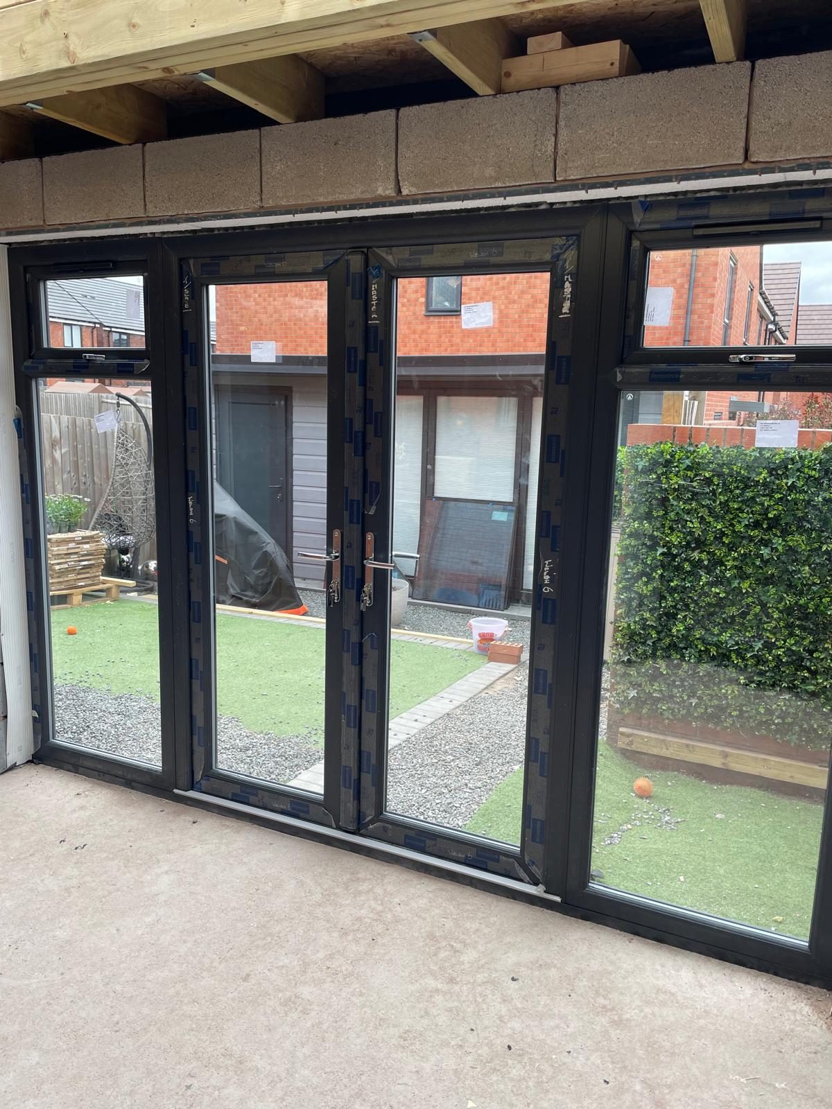 Interior of a house extension with dark aluminium bi-fold doors and exposed roof joists