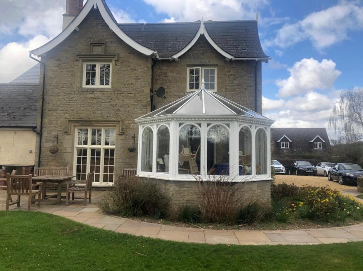 Original white timber conservatory with glazed pitched roof on a stone cottage before replacement