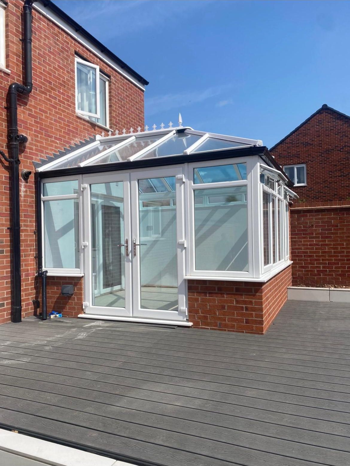 Completed white conservatory with glazed roof and French doors beside a brick house in Cannock