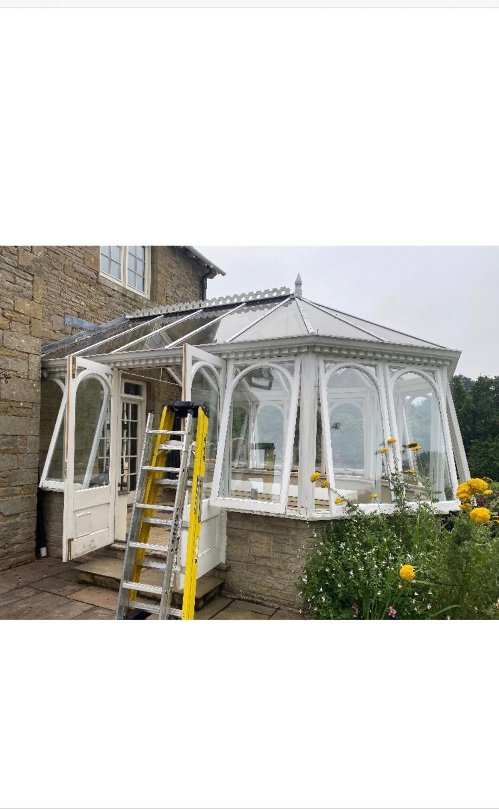 Old white conservatory being stripped out with ladders in place and glazing panels removed