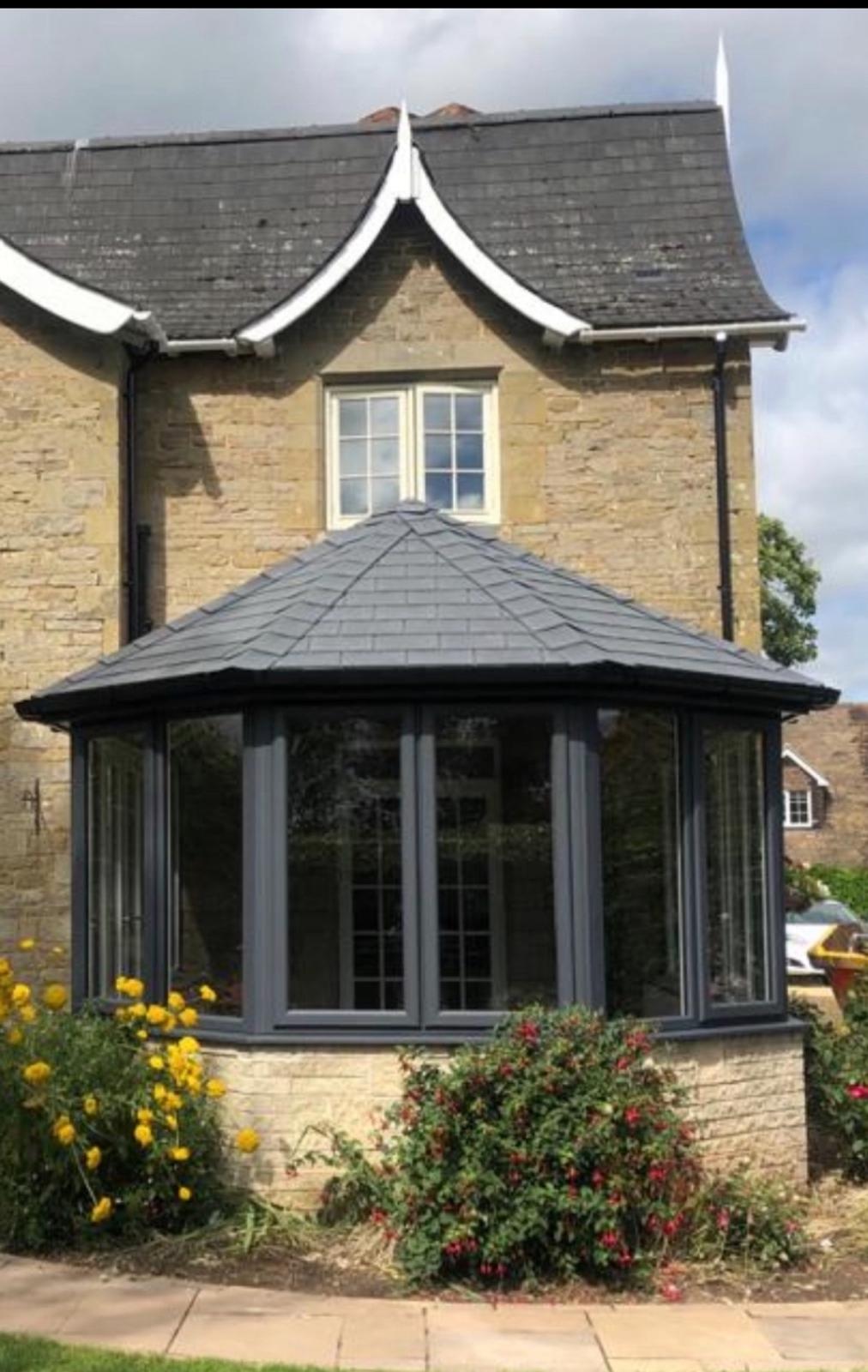 Finished grey framed conservatory with a tiled roof and bay windows built onto the stone elevation